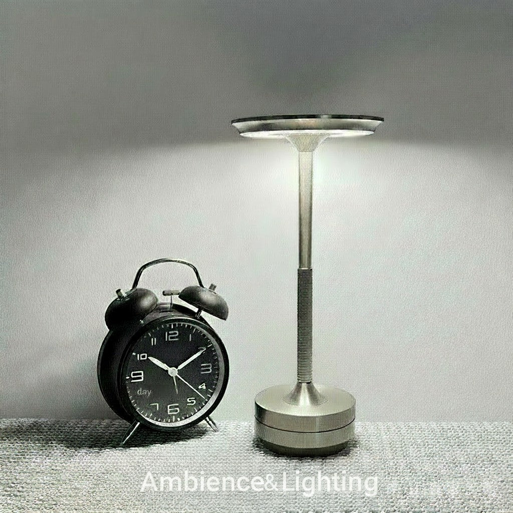 Srebrna lampa dotykowa LED NovaPulse o minimalistycznym designie z aluminiowym kloszem obok czarnego budzika